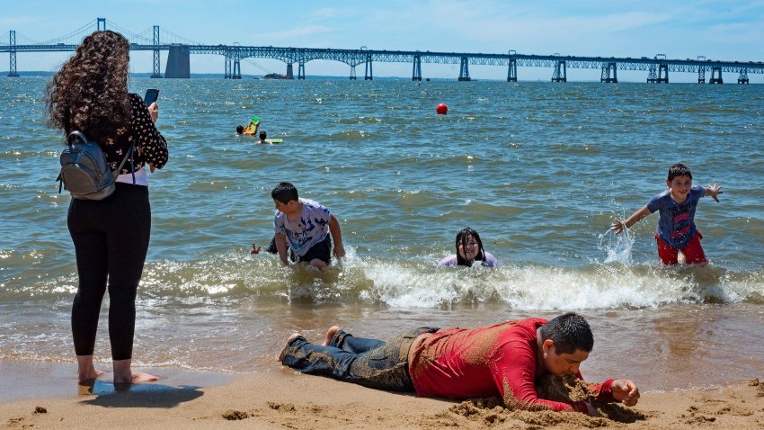 A man lies on the beach as his family plays in the Chesapeake Bay trying to escape the heat at Sandy Point State Park in Annapolis, Maryland on June 29, 2021. – The scorching heat — which is breaking records in Canada and the United States dating back more than 80 years — has been blamed on a high-pressure ridge trapping warm air in the region. (Photo by JIM WATSON / AFP) (Photo by JIM WATSON/AFP via Getty Images)